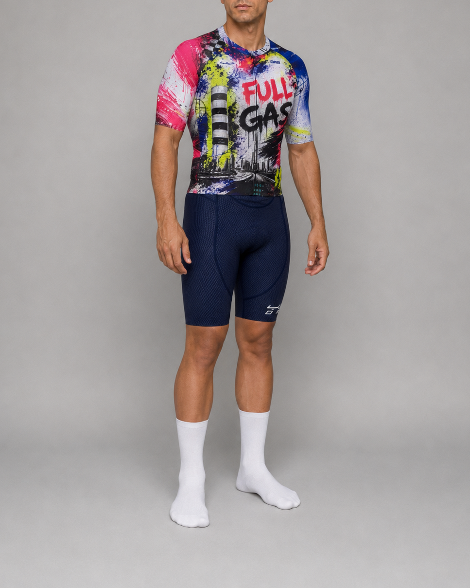 A man modeling a short-sleeve cycling jersey and matching navy cycling shorts against a neutral gray studio background. The jersey features a vibrant graffiti-style multicolor print with 'FULL LAS VEGAS' text, paired with navy shorts and white crew socks.